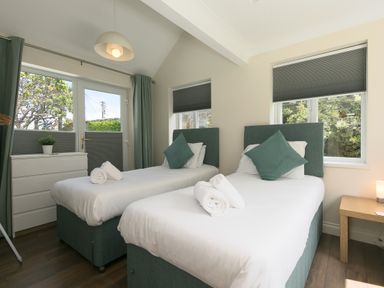 A bedroom with two single beds with green headboards and pillows a white dresser a wooden nightstand and windows with gray blinds at Spernenwyn in St Ives