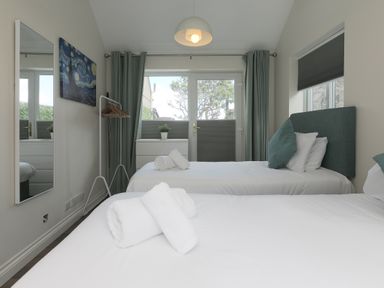 A bedroom with two single beds white linens and teal pillows a dresser a full length mirror and a clothes rack at Spernenwyn in St Ives