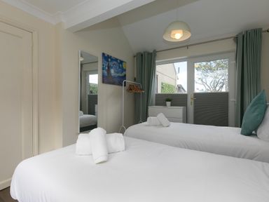 A bedroom with two single beds white bedding a mirror artwork curtains and a chest of drawers at Spernenwyn in St Ives
