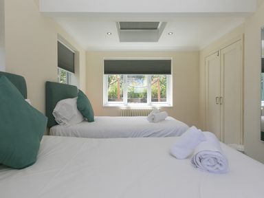 A bedroom with two single beds with white linens and green pillows a window with blinds and a wardrobe at Spernenwyn in St Ives