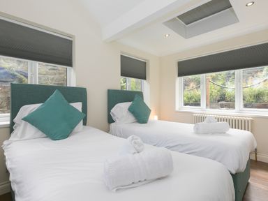 A bedroom with two single beds with teal headboards and pillows and rolled white towels on each bed at Spernenwyn in St Ives