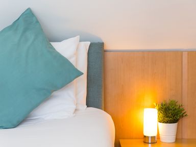 A bed with white and teal pillows next to a wooden bedside table with a lamp and a potted plant at Spernenwyn in St Ives