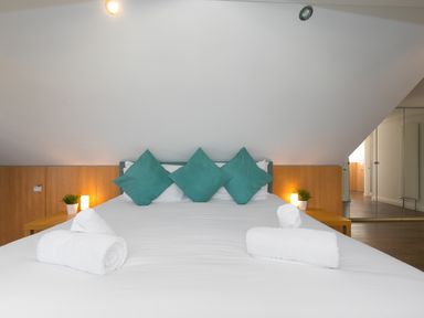 A bedroom with a large bed three teal pillows white towels on bed wooden side tables with lamps and plants at Spernenwyn in St Ives