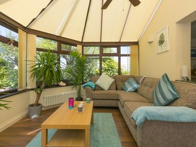 A conservatory with a brown sofa with blue cushions and a wooden coffee table with mugs and plants at Spernenwyn in St Ives