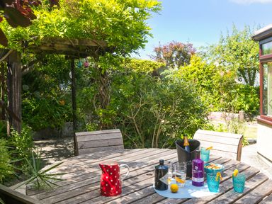 An outdoor wooden table with drinks glasses bottles and a red pitcher in a garden at Spernenwyn in St Ives