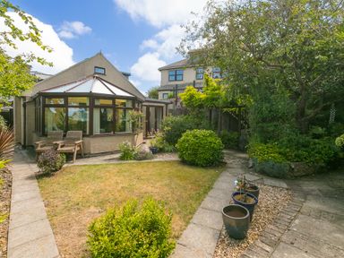A garden with a paved pathway shrubs and potted plants near a conservatory at Spernenwyn in St Ives