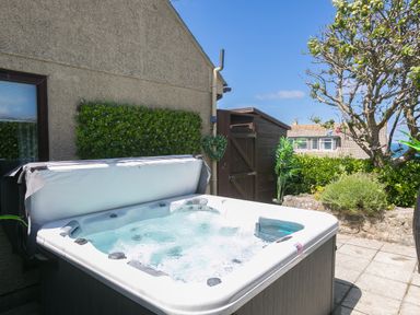 An outdoor patio area with a bubbling hot tub next to a building and garden at Spernenwyn in St Ives