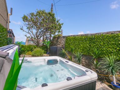 An outdoor hot tub surrounded by plants and a stone wall at Spernenwyn in St Ives
