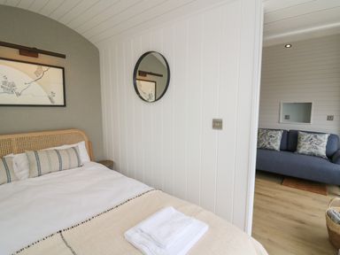 A bedroom with a bed and a round mirror on the wall next to a sitting area with a blue sofa at Ceunant in Llanfihangel-y-Creuddyn near Aberystwyth