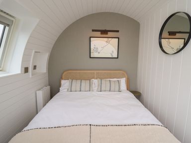 A bedroom with a bed and two cushions a round mirror and a framed picture on the wall at Ceunant Llanfihangel-y-Creuddyn near Aberystwyth