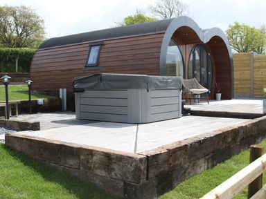An outdoor patio area with a hot tub and chair next to a rounded wooden cabin at Ceunant in Llanfihangel-y-Creuddyn near Aberystwyth