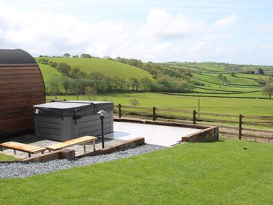 An outdoor hot tub on a paved area with a wooden bench and green fields in the background at Ceunant Llanfihangel-y-Creuddyn near Aberystwyth