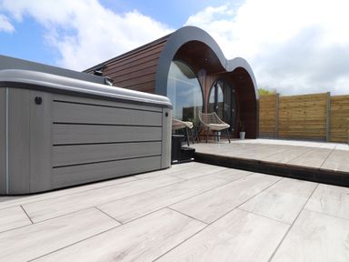 An outdoor patio with a hot tub two chairs and a modern curved wooden building with large windows at Ceunant Llanfihangel-y-Creuddyn near Aberystwyth