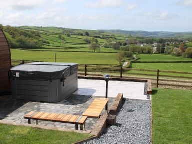 An outdoor area with a hot tub wooden benches and gravel path overlooking green fields at Ceunant Llanfihangel-y-Creuddyn near Aberystwyth