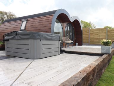 A wooden pod with curved roof on a tiled patio with a hot tub and outdoor chairs at Ceunant in Llanfihangel-y-Creuddyn near Aberystwyth