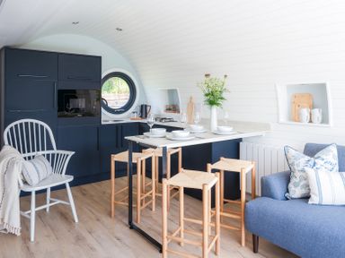 A kitchen and dining area with a round window wooden stools and a blue sofa at Ceunant in Llanfihangel-y-Creuddyn near Aberystwyth