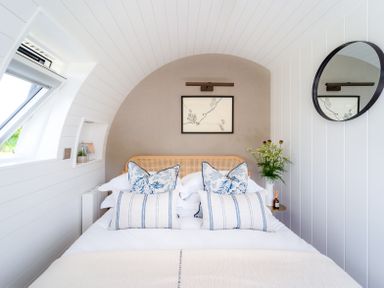 A bedroom with a bed with patterned pillows a round mirror and a wall art at Ceunant in Llanfihangel-y-Creuddyn near Aberystwyth