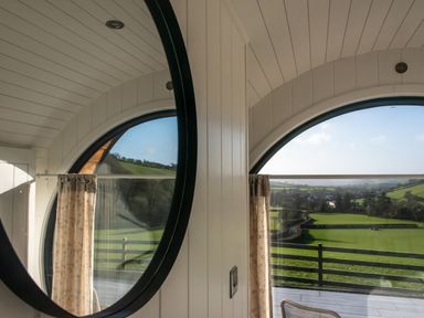 A circular window with curtains showing a view of green fields and hills at Ceunant Llanfihangel-y-Creuddyn near Aberystwyth