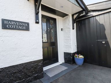 The front door entrance with a doormat and flower pot next to a black gate at Harvenna Cottage in Crackington Haven
