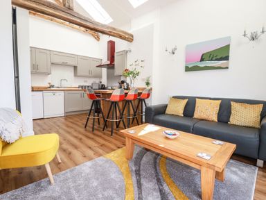 An open plan kitchen and living room with grey cabinets a wooden countertop and a black sofa at Harvenna Cottage in Crackington Haven