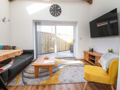A living room with a black sofa yellow chair wooden coffee table and wall clock with glass door to outside at Harvenna Cottage in Crackington Haven