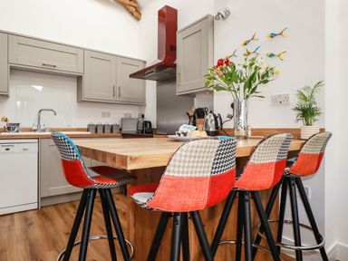 A kitchen with a wooden island and colorful bar stools at Harvenna Cottage in Crackington Haven