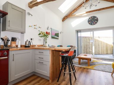 A kitchen area with wooden countertops and stools next to a living room with a coffee table and sliding glass doors at Harvenna Cottage in Crackington Haven