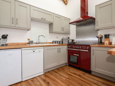 A kitchen with grey cabinets a red oven wooden countertops and wood flooring at Harvenna Cottage in Crackington Haven
