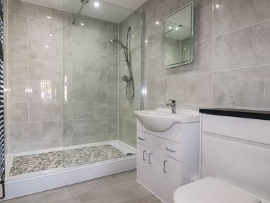 A bathroom with a shower, sink with cabinet, mirror, and toilet at Harvenna Cottage in Crackington Haven