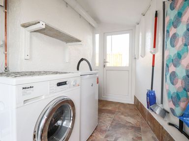 A laundry room with a washing machine dryer broom and ironing board at Harvenna Cottage in Crackington Haven