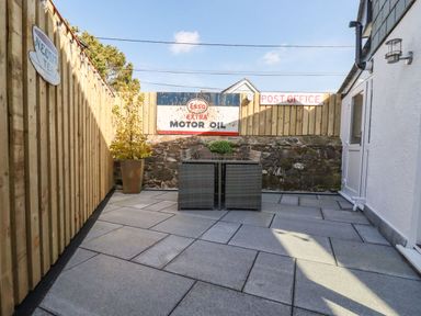A fenced patio area with a small table and chairs and vintage signs on the fence at Harvenna Cottage in Crackington Haven