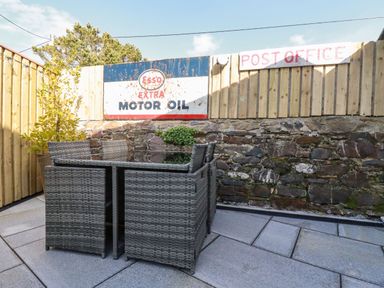 An outdoor patio with a wicker dining set and vintage signs on a wooden fence at Harvenna Cottage in Crackington Haven