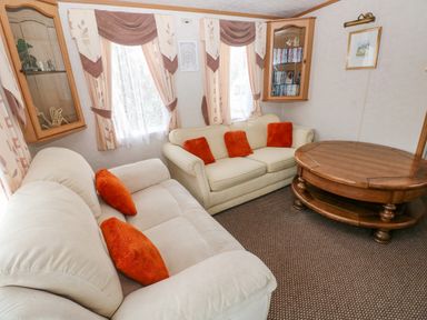 A living room with two sofas with orange pillows a wooden coffee table and wall cabinets at Park Lane in Llanteg near Kilgetty
