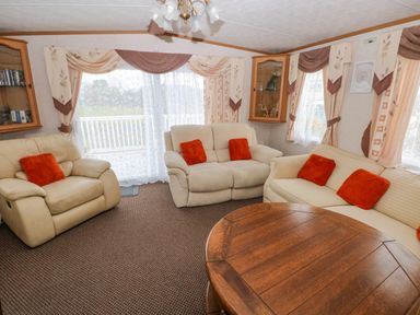 A living room with three sofas and orange cushions and a wooden coffee table at Park Lane in Llanteg near Kilgetty