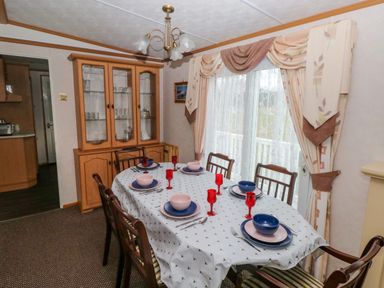 A dining room with a table set for six next to a cabinet and window with curtains at Park Lane in Llanteg near Kilgetty