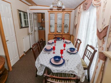 A dining room with a set table with bowls and red glasses a china cabinet and patterned curtains at Park Lane in Llanteg near Kilgetty