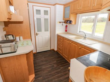 A kitchen with wooden cabinets a white sink a toaster and a door at Park Lane Llanteg near Kilgetty