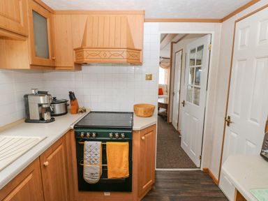 A kitchen with wooden cabinets a black stove an espresso machine and an open door showing a living area at Park Lane Llanteg near Kilgetty