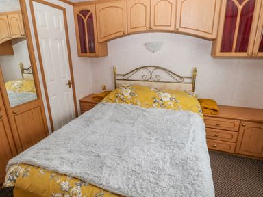 A bedroom with a bed covered by yellow floral bedding and a gray blanket at Park Lane in Llanteg near Kilgetty
