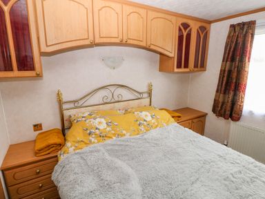 A bedroom with a bed with yellow floral bedding and gray blanket wooden cabinets above and bedside tables at Park Lane in Llanteg near Kilgetty