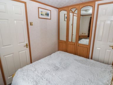 A bedroom with a bed covered in a white fluffy blanket a corner wardrobe with mirrored doors and two white doors on each side at Park Lane in Llanteg near Kilgetty