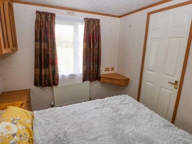 A bedroom with a bed covered in a gray blanket next to a window with patterned curtains and a white door at Park Lane in Llanteg near Kilgetty