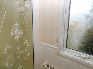 A bathroom corner with a frosted window with leaf patterns a beige and white tiled wall and a glass shower door with white ornamental designs at Park Lane in Llanteg near Kilgetty