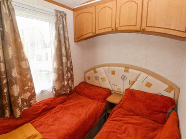 A bedroom with two single beds with red covers a window with curtains and wall cabinets at Park Lane in Llanteg near Kilgetty