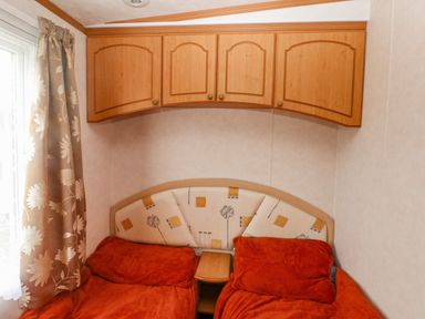 A bedroom with two single beds under wooden cupboards and a window with floral curtains at Park Lane in Llanteg near Kilgetty