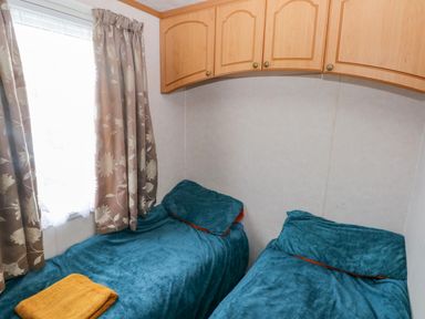 A small room with two single beds with blue blankets and a window with floral curtains at Park Lane in Llanteg near Kilgetty