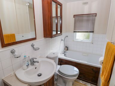 A bathroom with a sink toilet bathtub mirror cabinet and yellow towel at Park Lane in Llanteg near Kilgetty