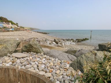 A pebble beach with rocks and a calm sea with houses along the shore at Park Lane in Llanteg near Kilgetty