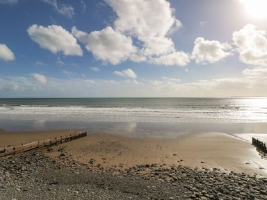 A beach with pebbles and wooden groynes under a partly cloudy sky at Park Lane in Llanteg near Kilgetty