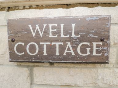 A wooden sign with the text Well Cottage mounted on a stone wall at Well Cottage Nr Malmesbury